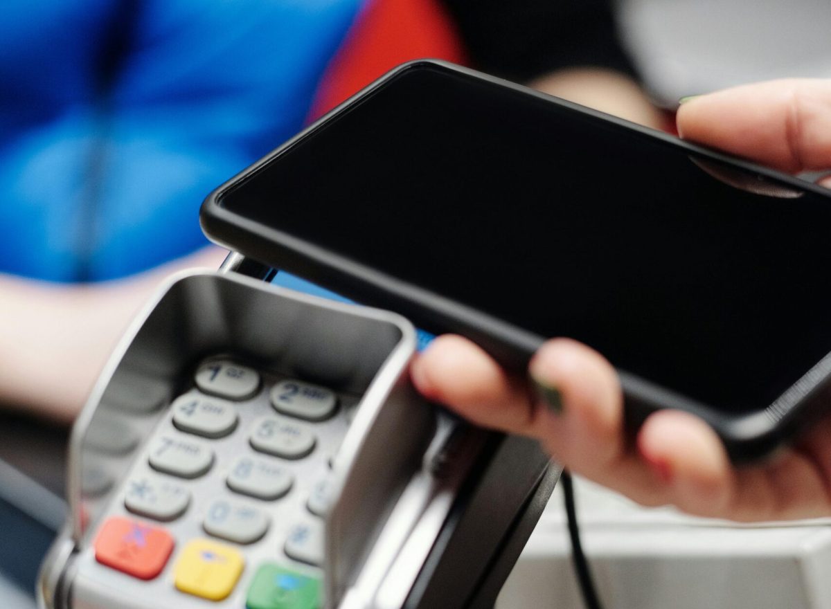 Close-up of a hand making contactless payment using a smartphone at a card terminal.
