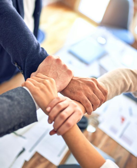 Close-up of diverse hands joining together over a table in an office setting, symbolizing teamwork and cooperation.